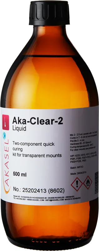 Akasel Aka-Clear-2 Liquid, 500 ml: Brun glasflaska med gul kork som innehåller vätska för ett tvåkomponents akrylsystem. Etiketten visar produktnamnet, artikelnummer 25202413 (8602), samt information om snabb härdning och specifika användningsinstruktioner. Speciellt utvecklad för metallografiska applikationer, idealisk för att skapa transparenta inbäddningar i kombination med Aka-Clear-2 Powder för noggrann analys och provberedning.