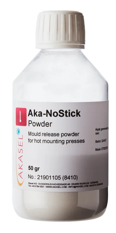 Akasel Aka-NoStick Powder i en genomskinlig plastflaska med vit skruvkork. Etiketten visar produktnamnet "Aka-NoStick Powder" och beskrivningen "Mould release powder for hot mounting presses." Ytterligare detaljer på etiketten: Innehåll 50 g, Artikelnummer 21901105 (8410), tillverkad i Danmark. Speciellt utvecklad för metallografiska varmpressar för att säkerställa enkel formsläpp av prover.